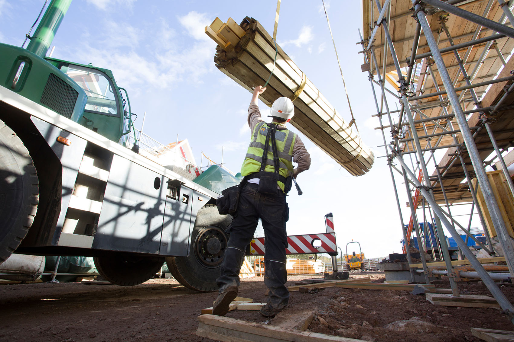 Construction worker on a building site standing near a crane carrying building supplies.