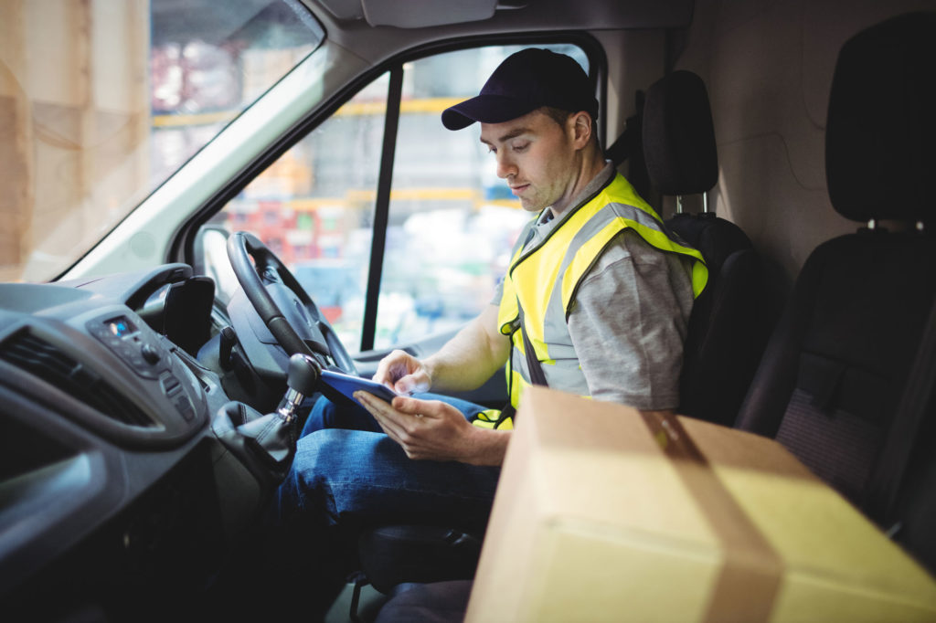 A delivery driver checks a tablet in a parked truck