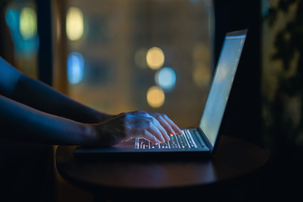 Shot of woman's hand typing on computer keyboard in the dark