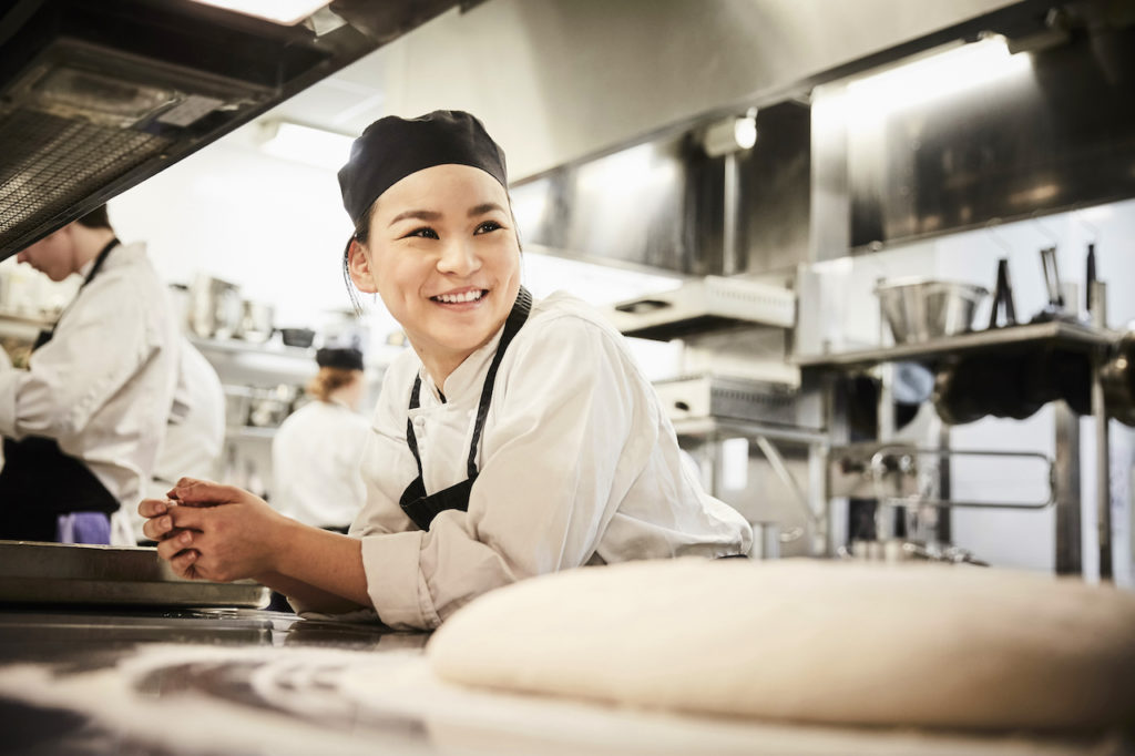 Smiling chef in uniform leaning on counter in commercial kitchen