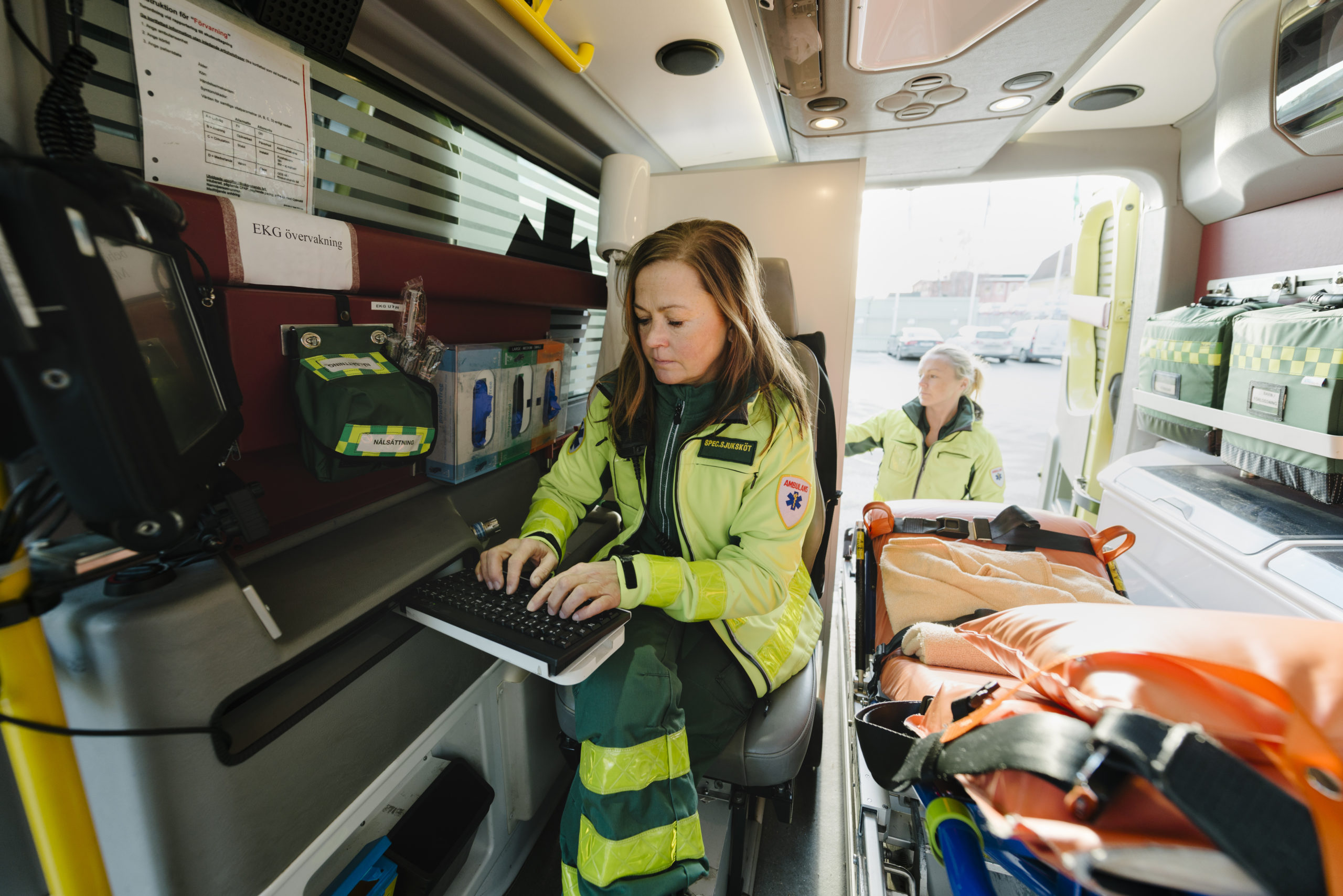 Paramedic using computer in ambulance while colleague standing in background