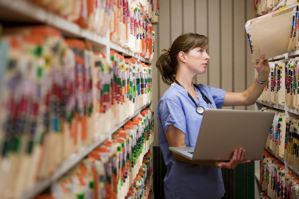 Nurse comparing computer medical records to old paper records.