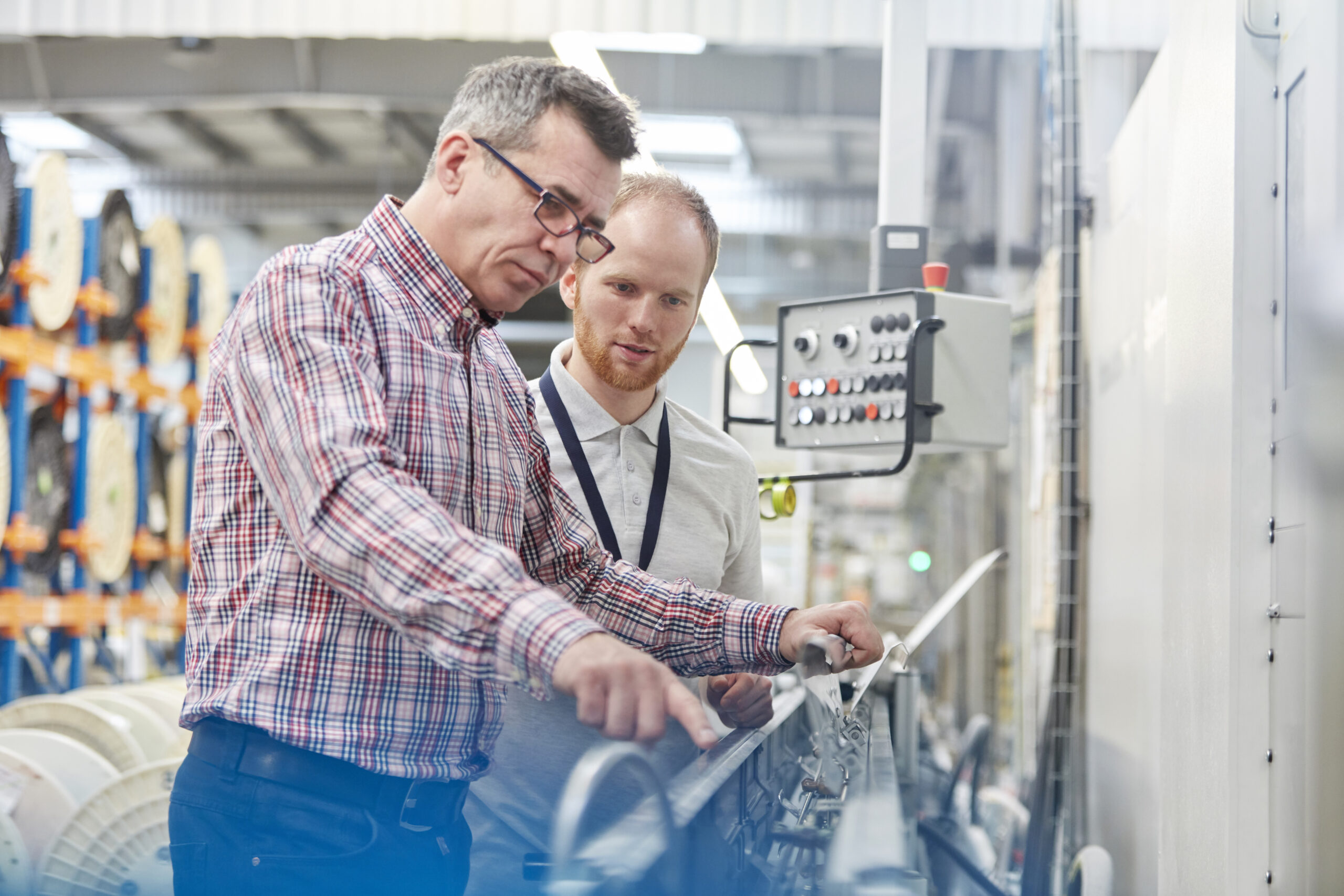 Supervisor and employees examining machinery in fiber optics factory