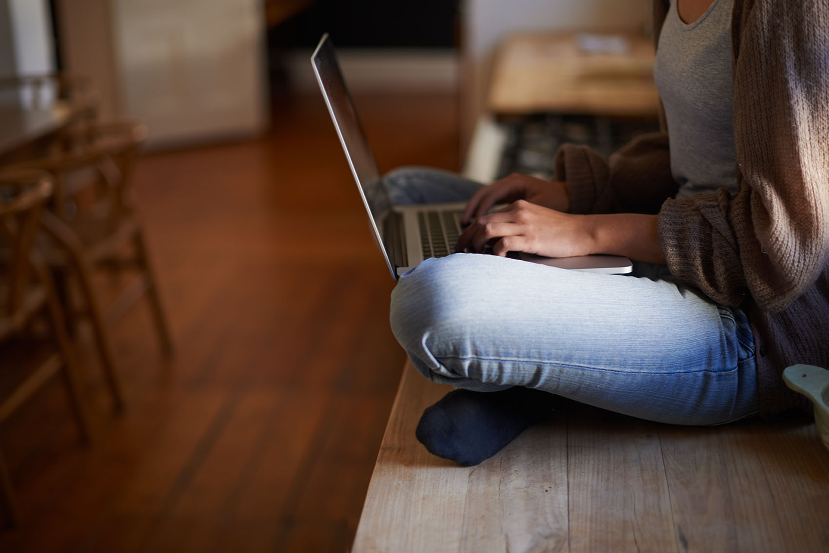 Cropped image of a woman sitting on a counter typing on her laptop