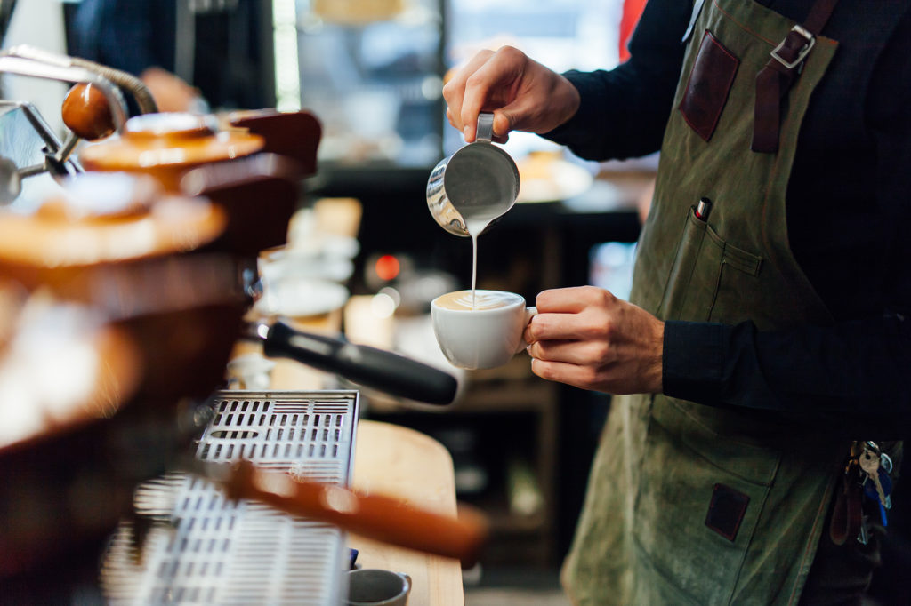 Barista in einem Cafè schüttet aufgeschäumte Milch in eine Tasse.