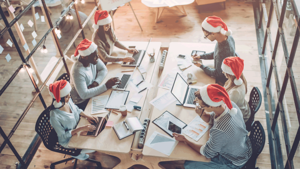A team of six people with santa hats on working in an open plan office on laptops and tablets.