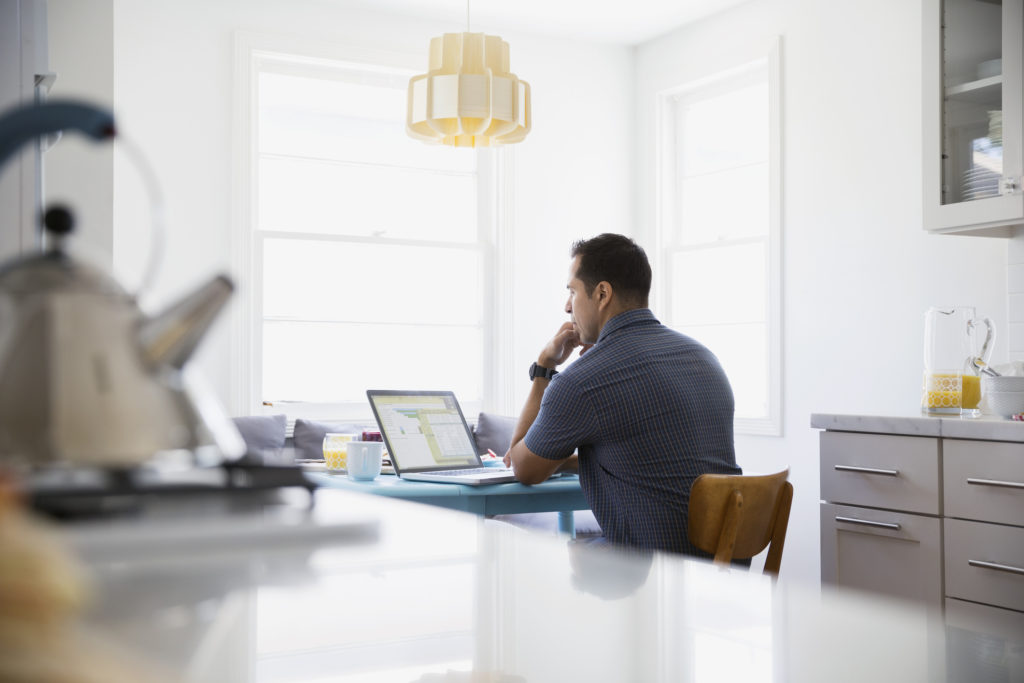 Man using laptop at kitchen table.