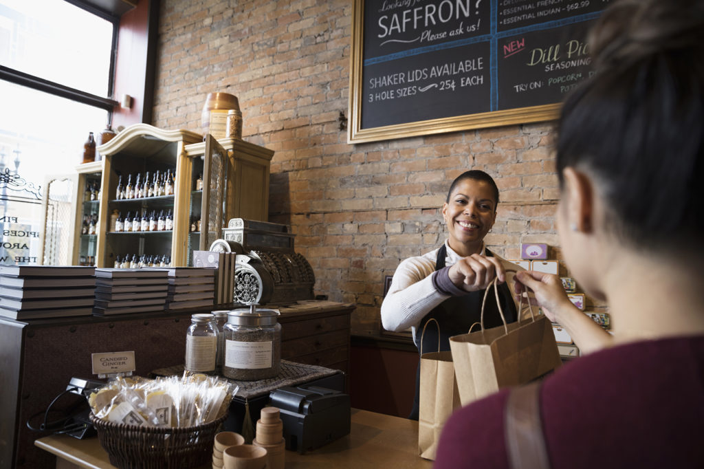 Smiling spice shop owner giving shopping bags to customer at counter