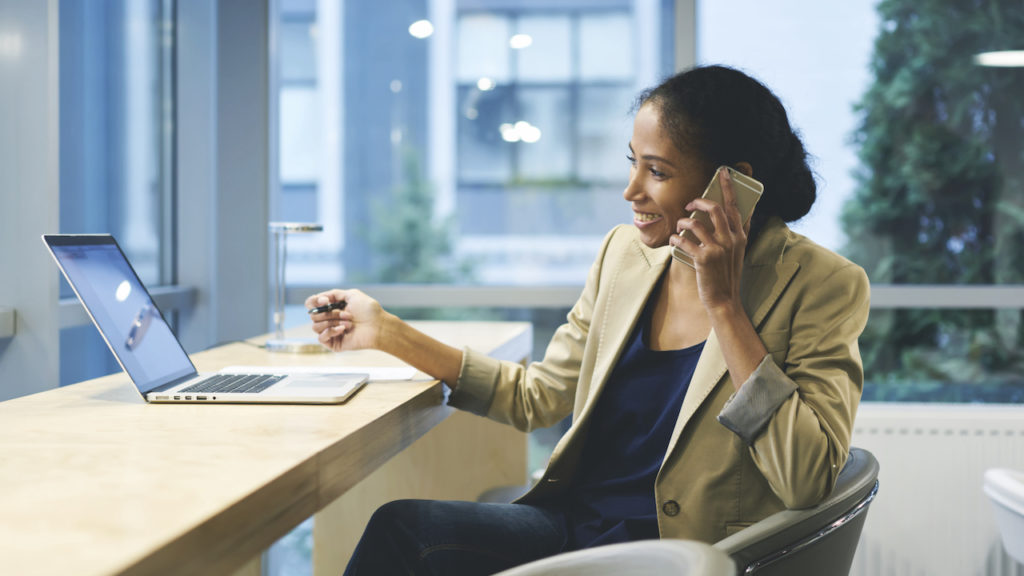 Photo of woman at desk in front of laptop smiling while talking on the phone