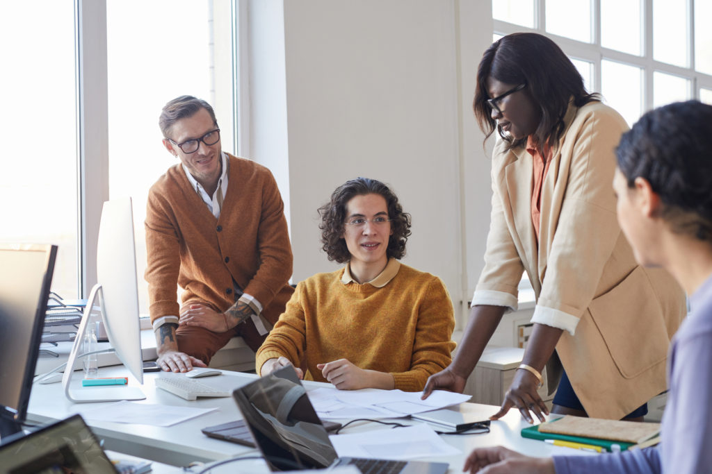 Portrait of coworkers discussing a project while using computers in modern office