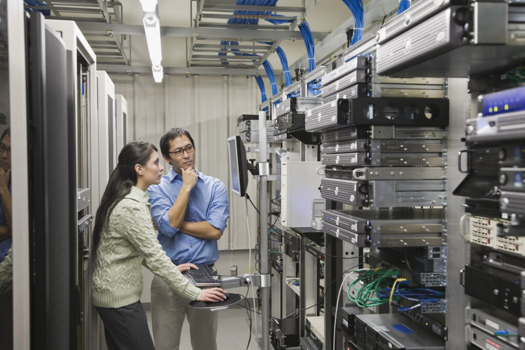 Coworkers looking intently at a computer screen in a server and equipment room