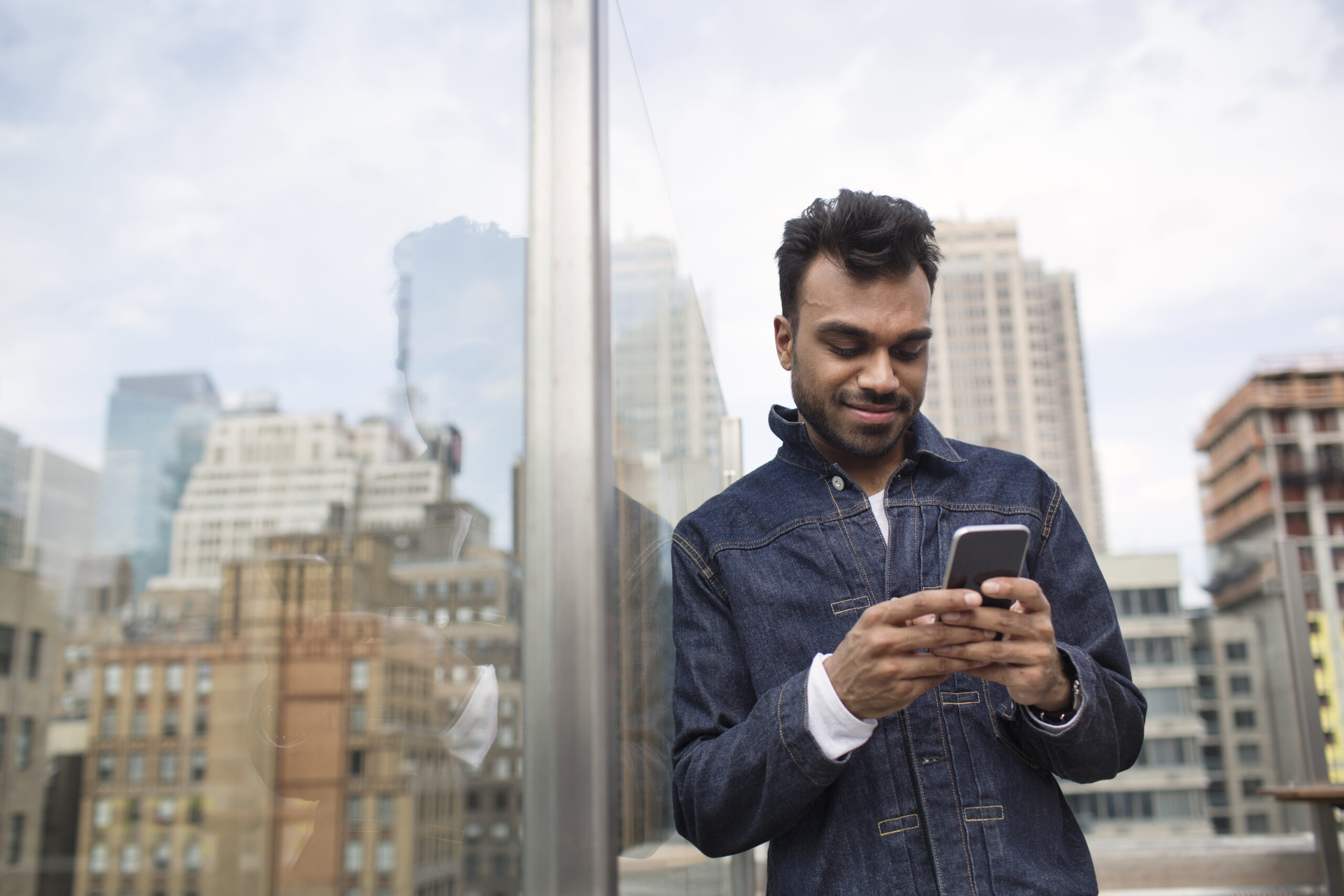 Smiling young person using phone while standing by window