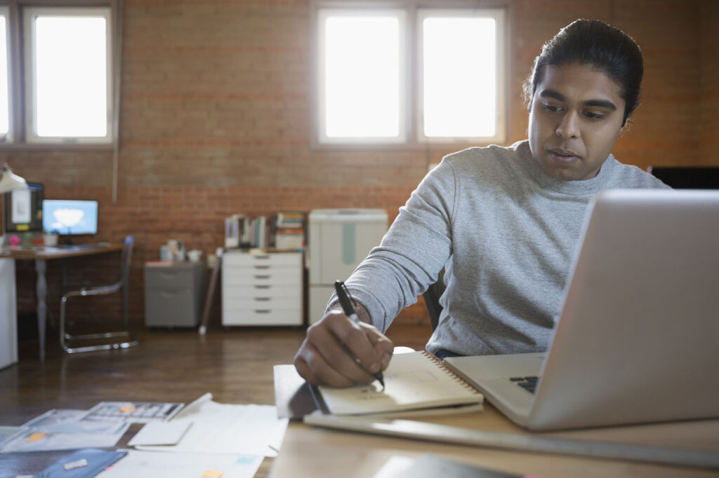Designer taking notes at laptop in office
