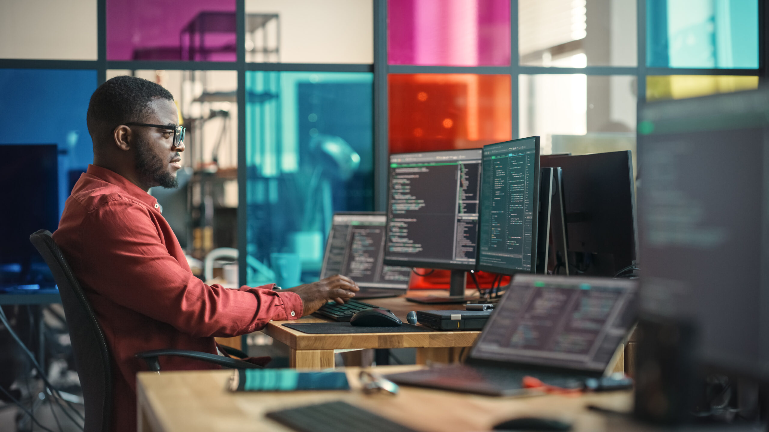 Person writing lines of code on desktop computer with multiple monitors and laptop in office