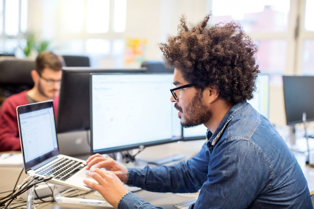 Portrait of young mixed race man at his desk working on laptop