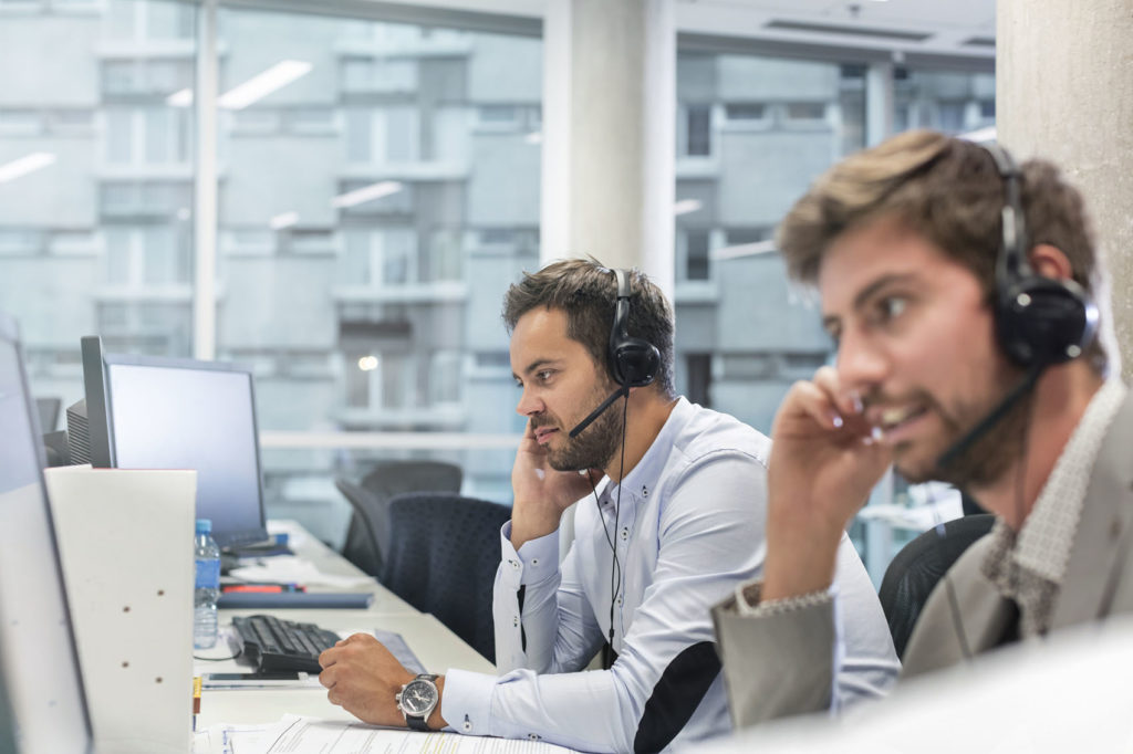 Professionnels équipés de dispositifs mains libres parlant au téléphone et travaillant sur des ordinateurs dans un bureau.