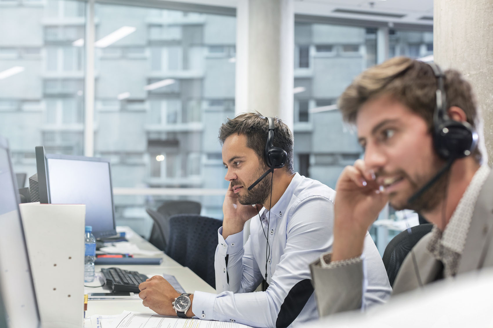 Customer service employees with hands-free devices talking on telephone working at computers in office.