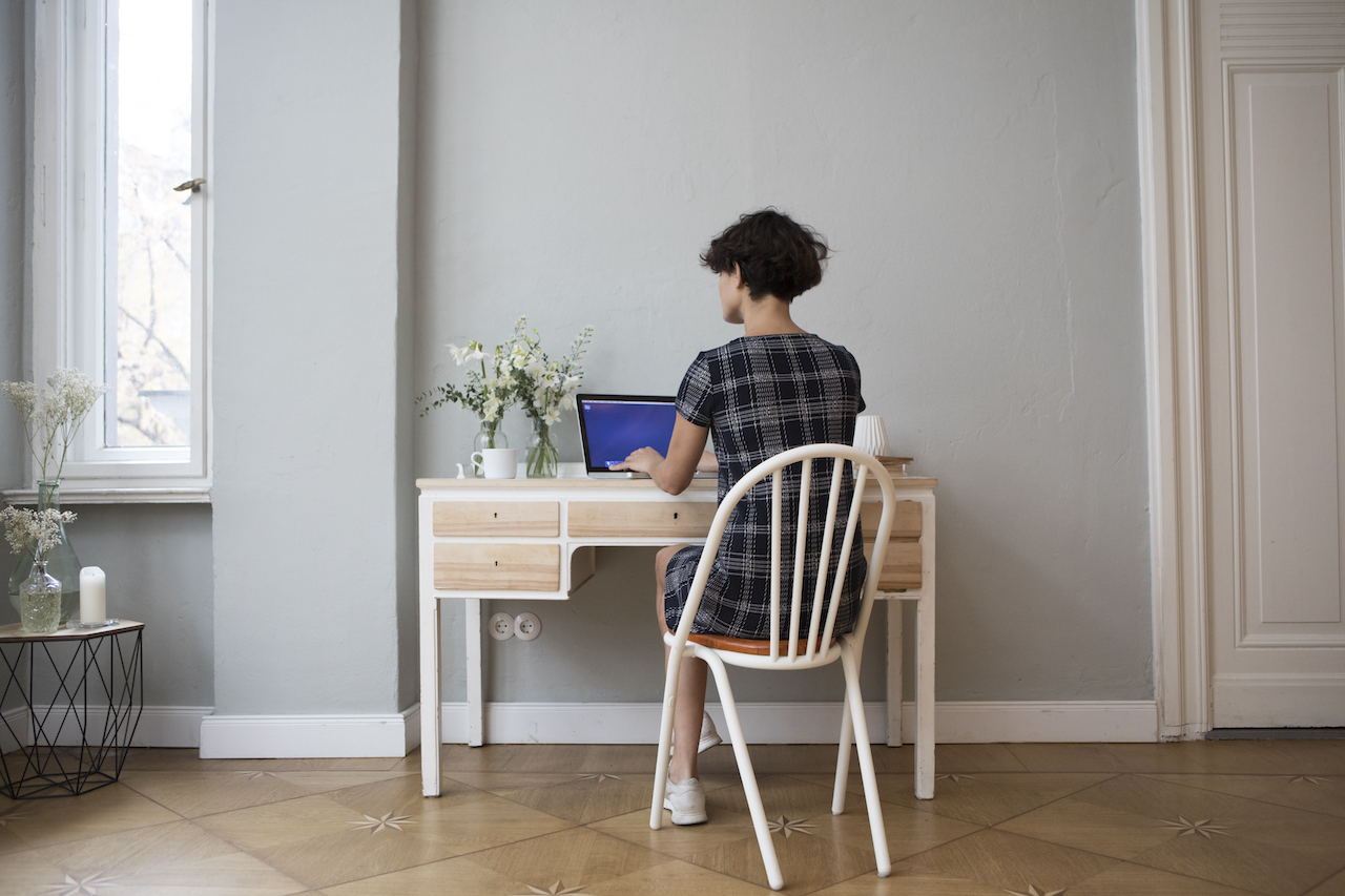 Back view of young woman sitting at desk at home using laptop