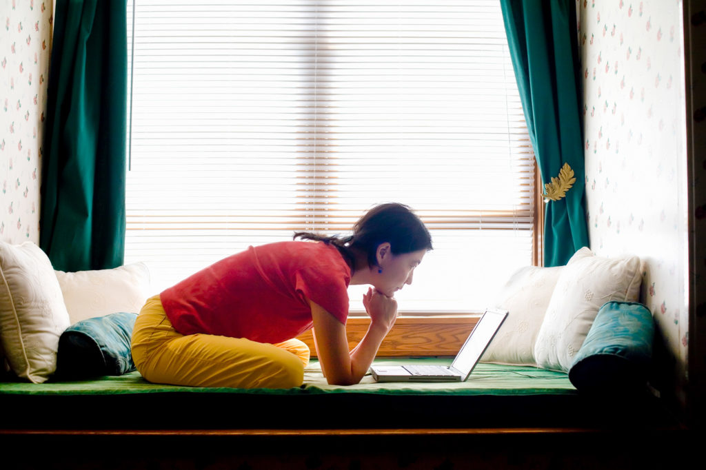 Woman sits on couch at home searching at her laptop 