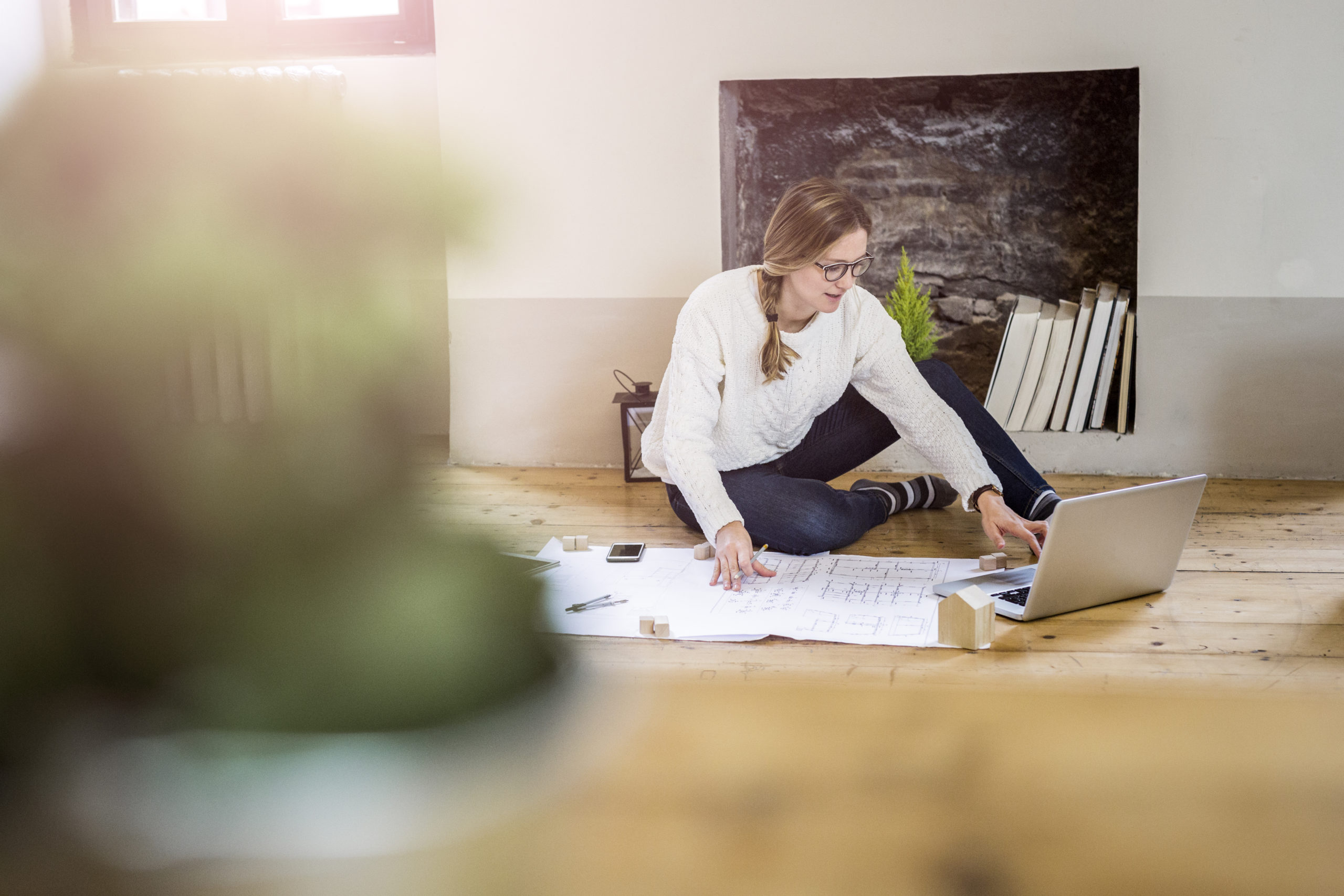 Person working on floor with blueprint and laptop.