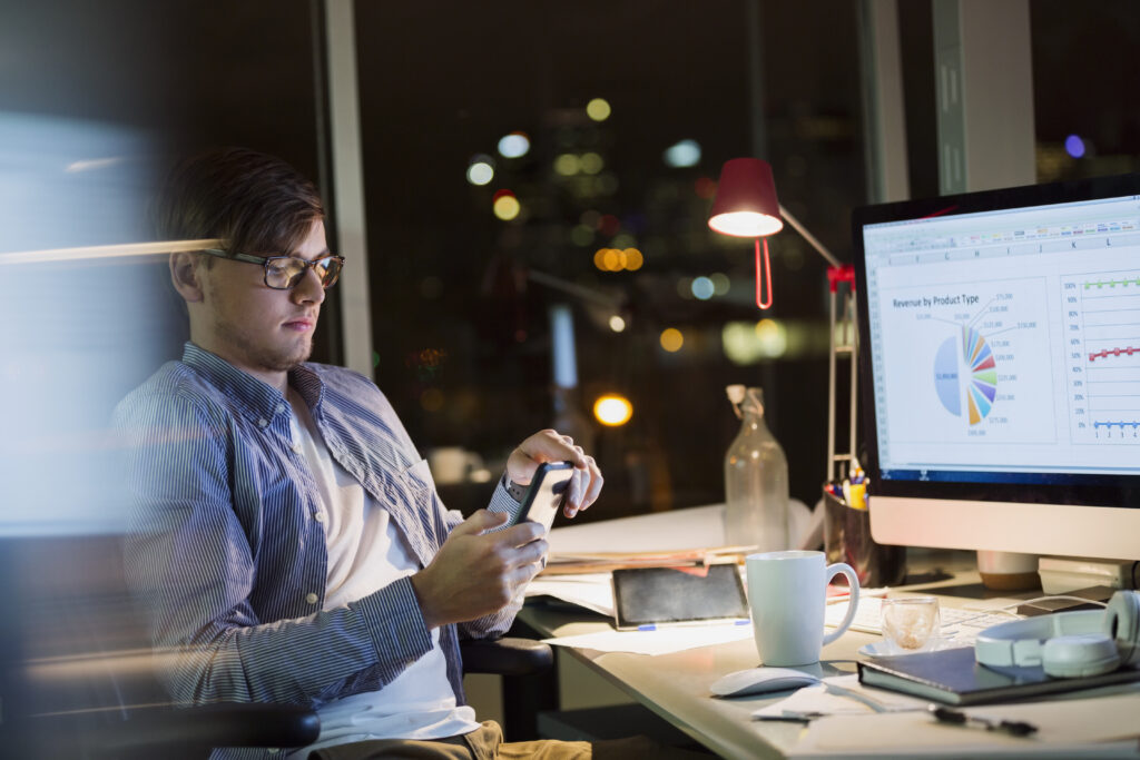 Young person looking at phone while working late in the office