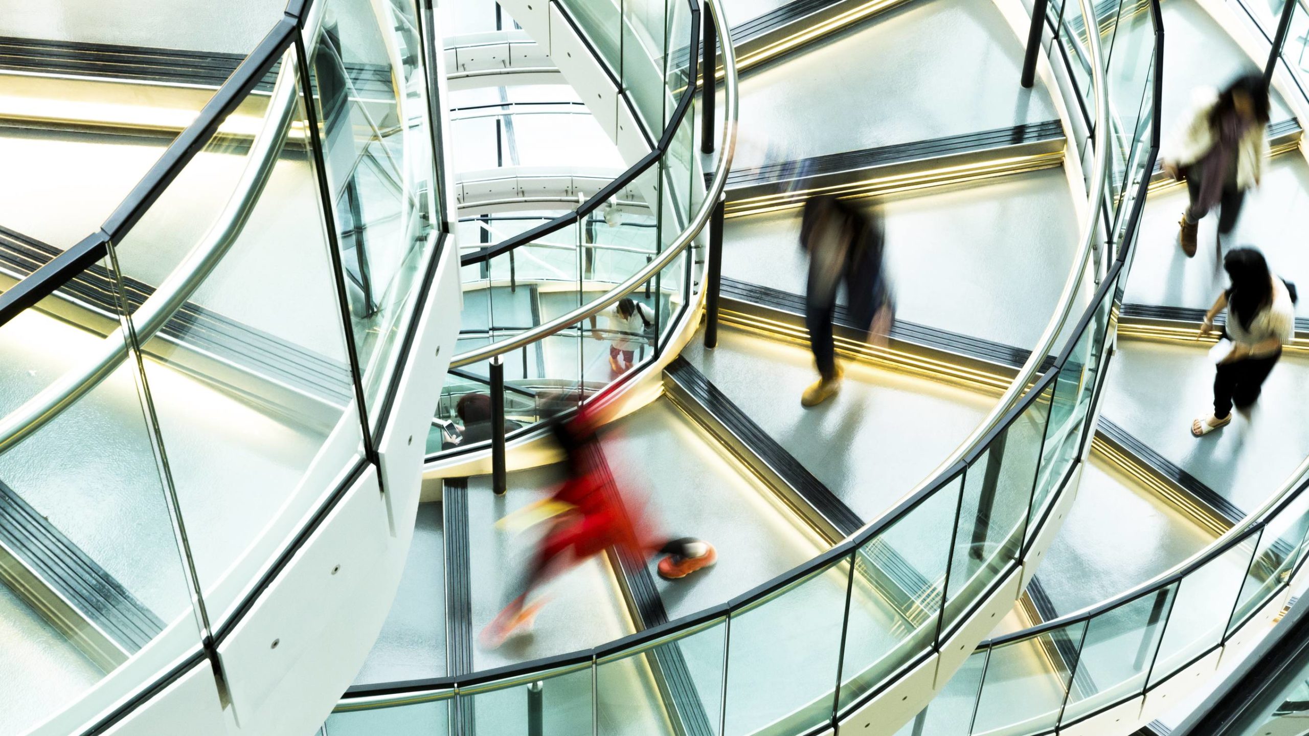 An out of focus aerial view of people going up and down a glass spiral staircase.