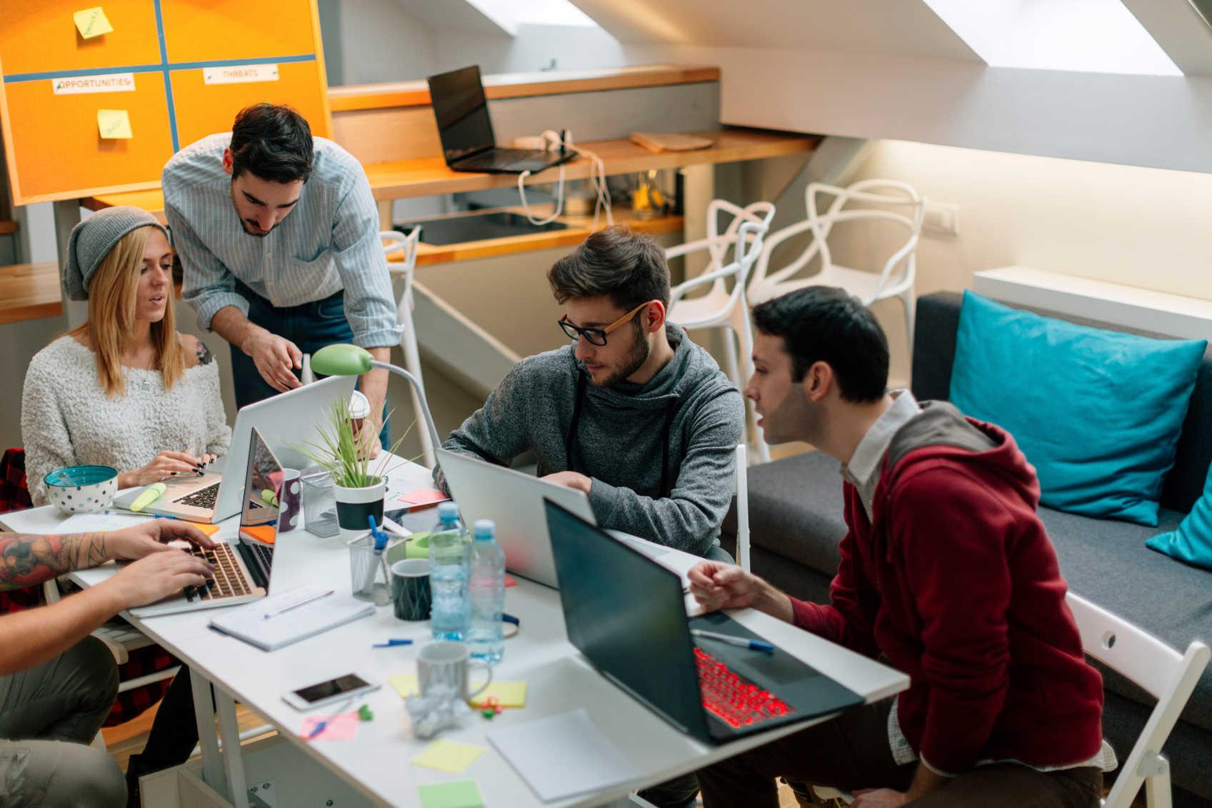 A team of people working together at a meeting table with multiple laptops open