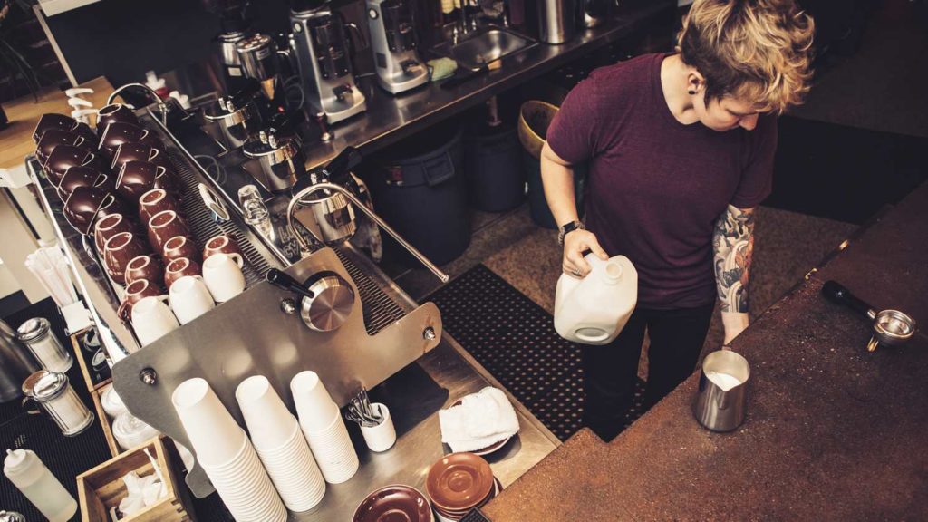 An aerial view of a barista making a coffee behind a cafe counter.