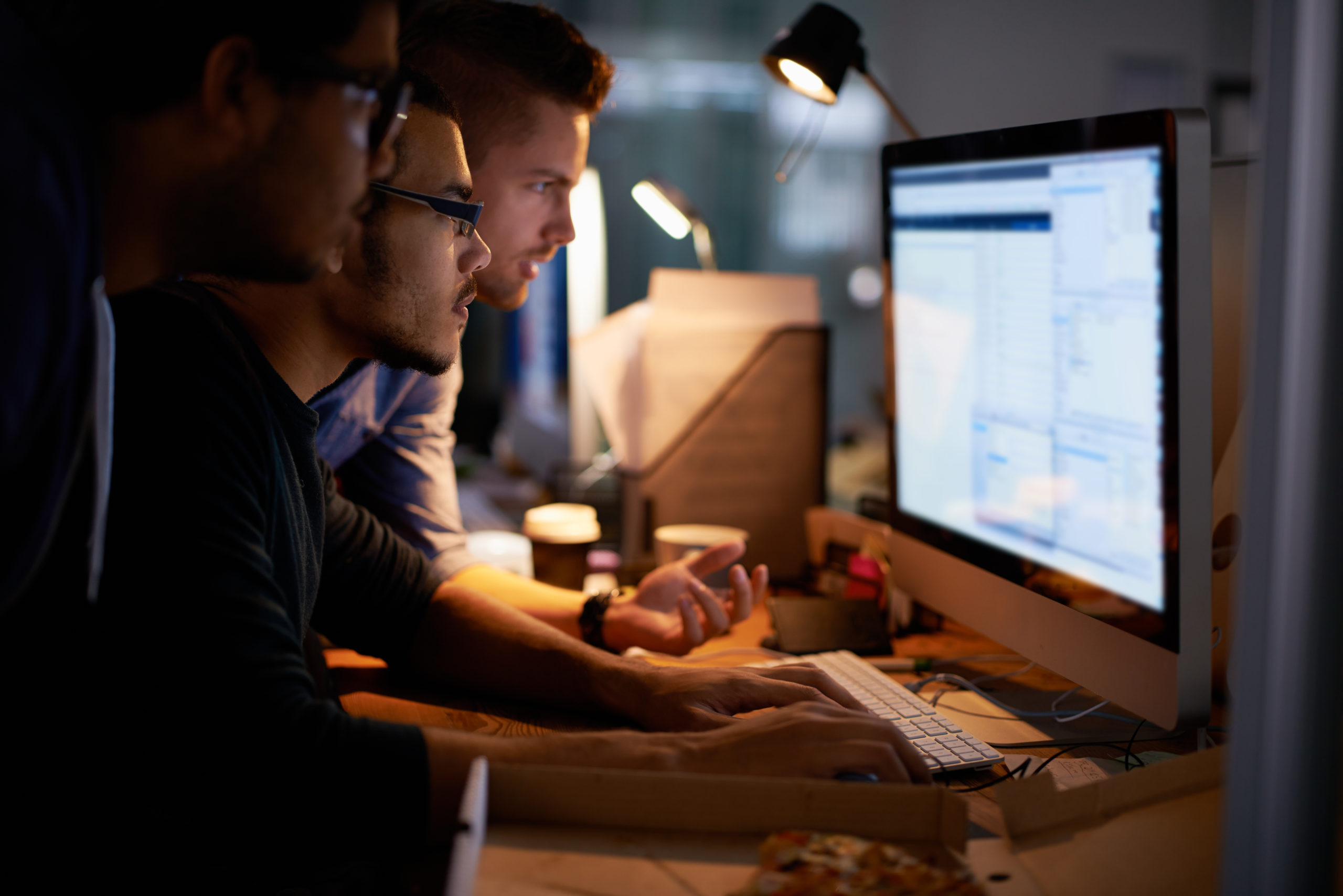 Three young workers gathered around one computer monitor