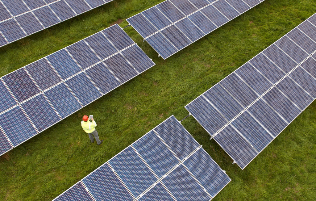 Aerial view of man in hard hat inspecting solar panels with clip board.