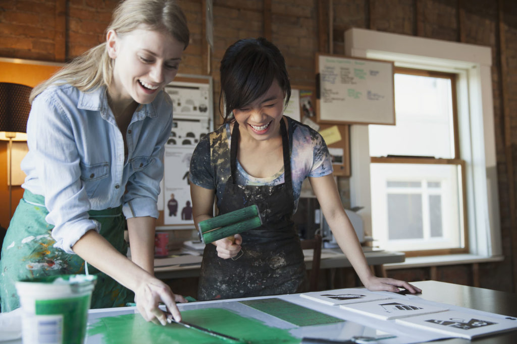 Happy female design professionals inking up etching plates for printmaking