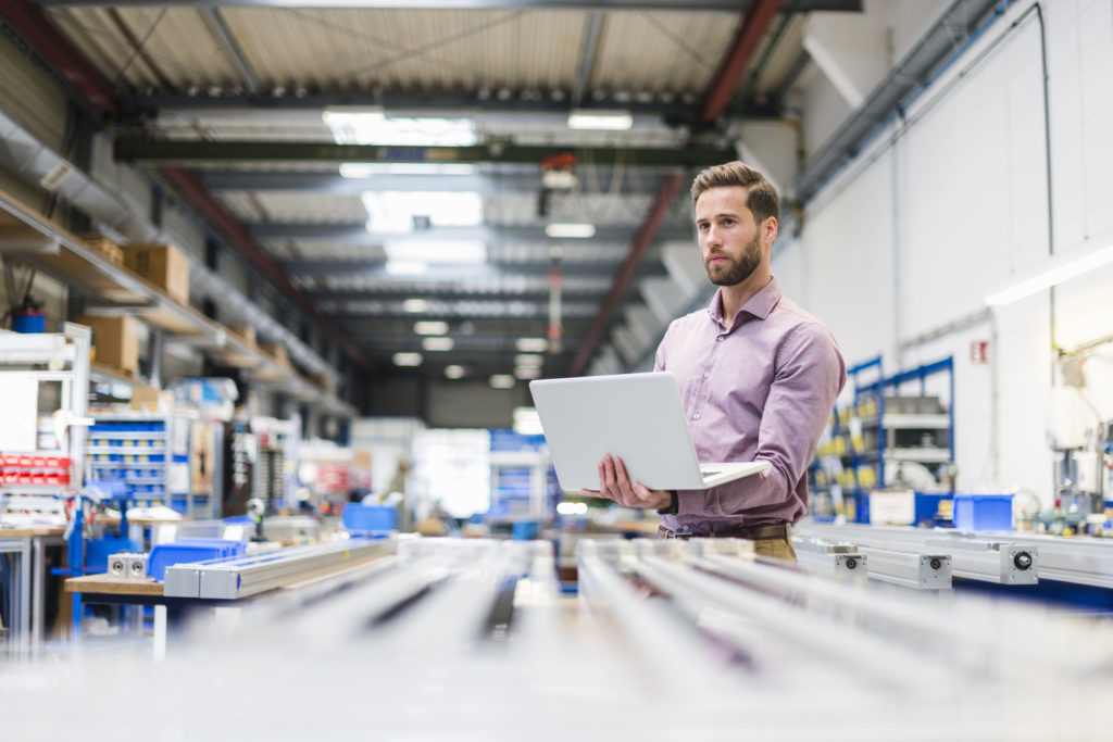 Young businessman using laptop in production hall.