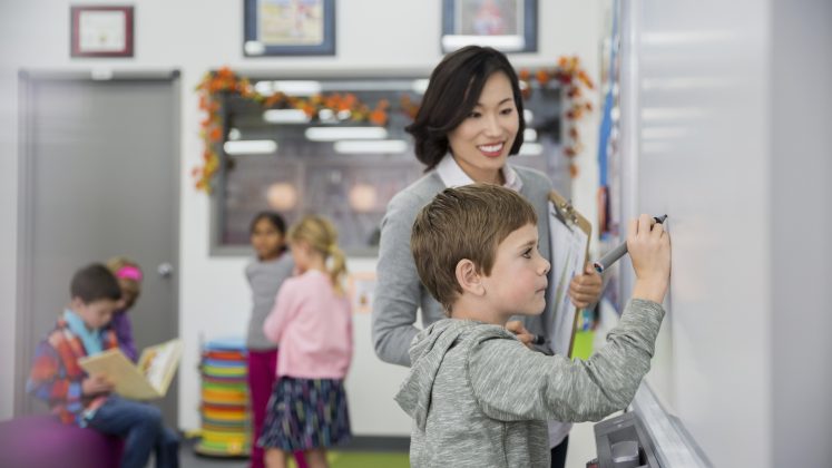 Teacher and young student writing on a whiteboard.