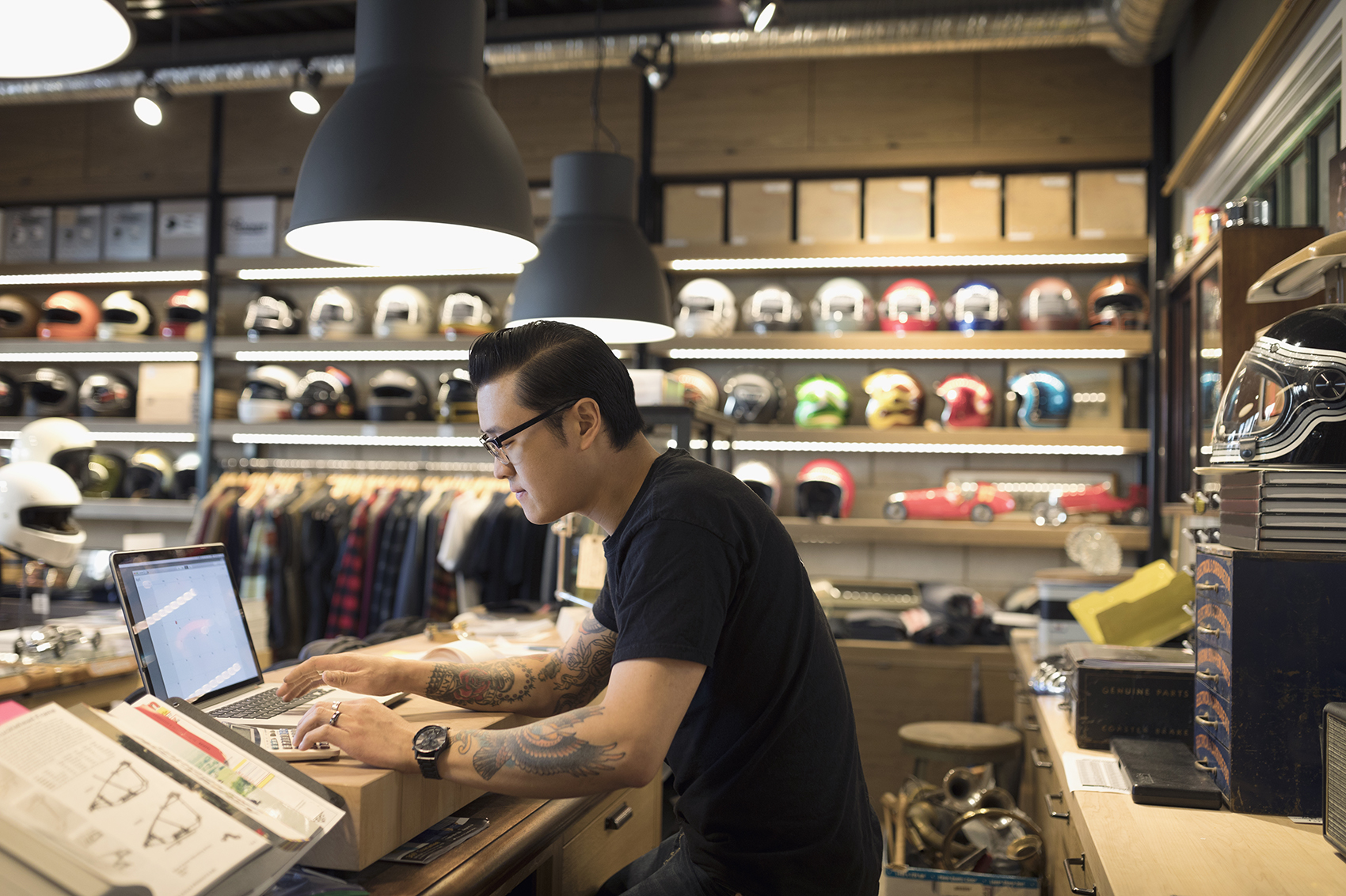 Motorcycle shop owner working at laptop behind counter.