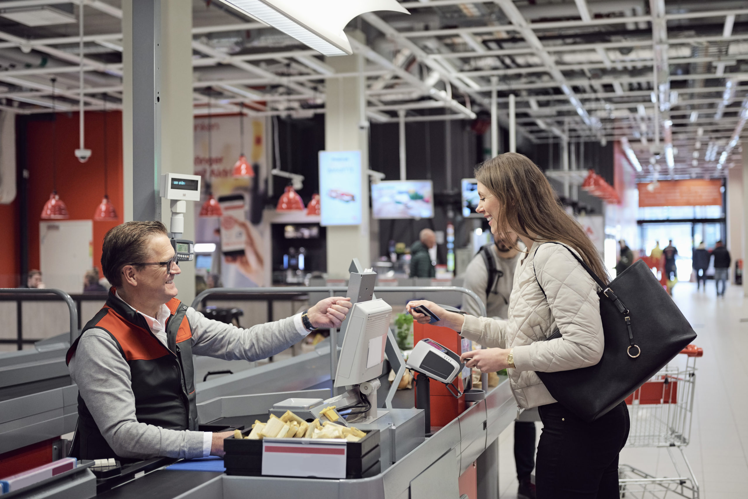 Mature cashier talking to woman while paying at checkout counter in supermarket.