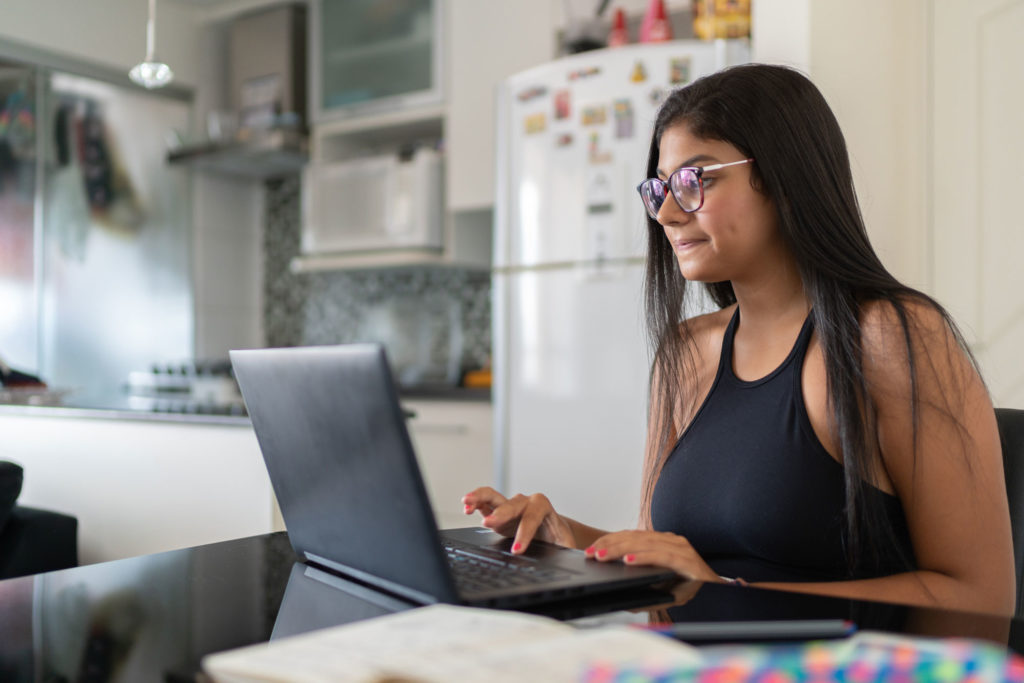 Woman working on a laptop at a kitchen table.