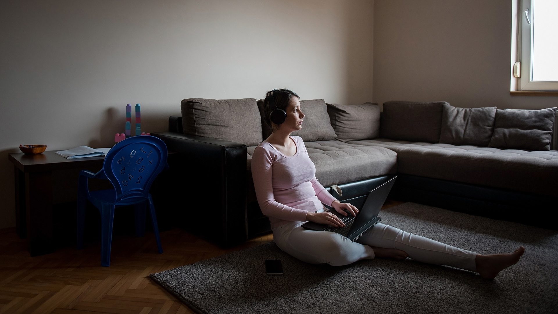 Person sitting on floor in dark living room on laptop
