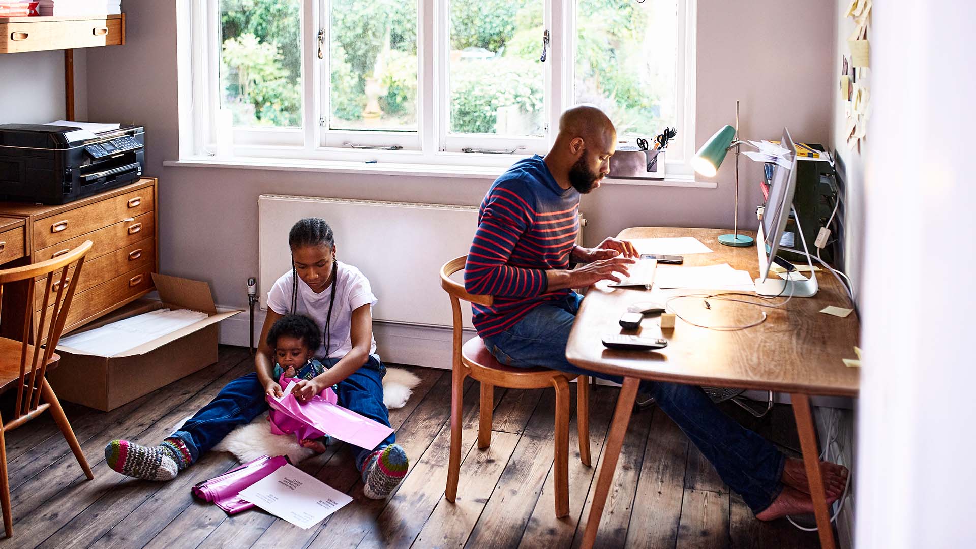 Dad sits at desk working while mom helps small child get ready for school