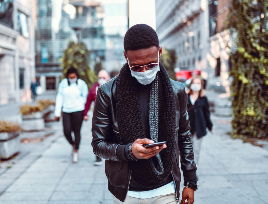 Man with mask walking down street looking at his phone