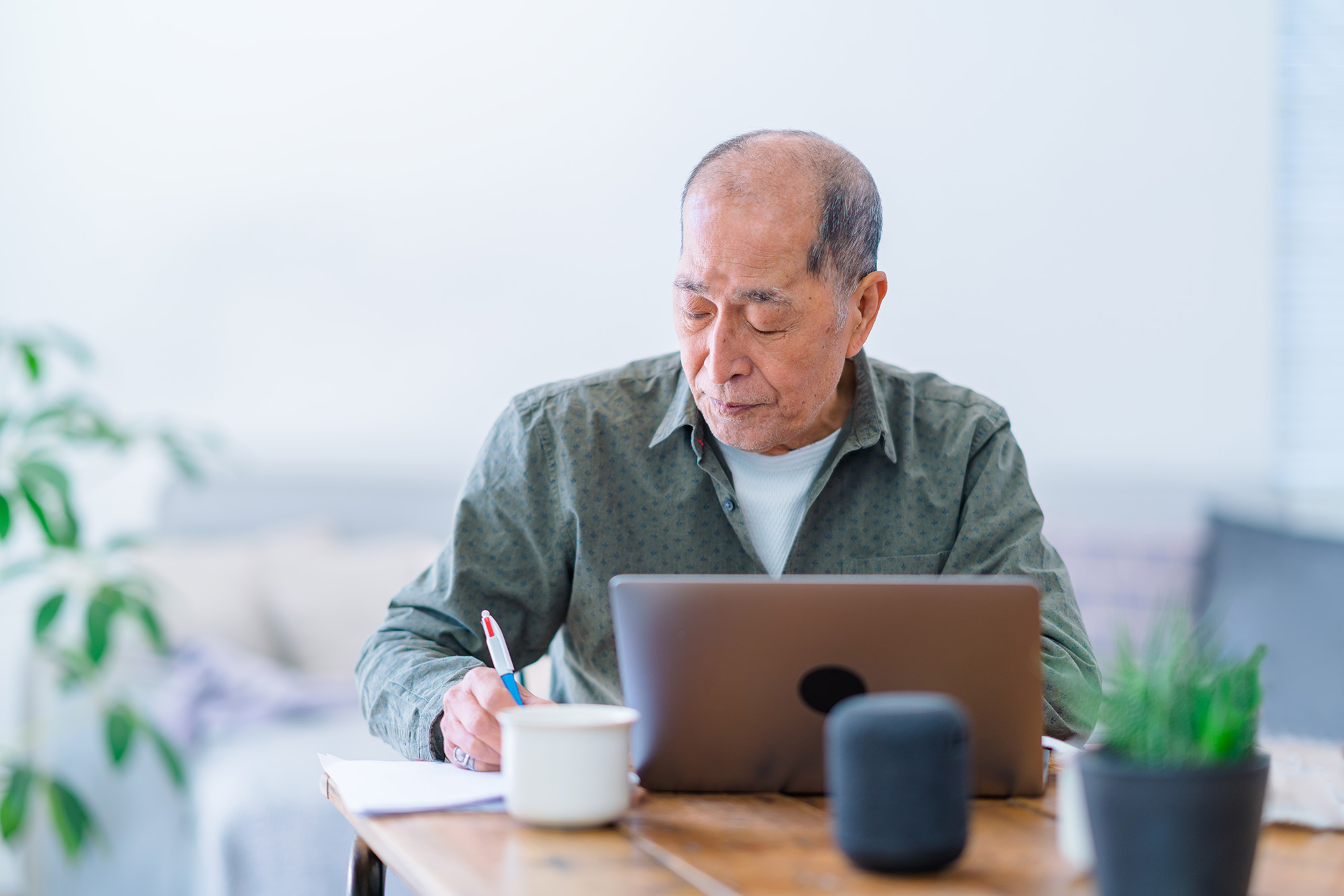 Person writing on notepad in front of laptop