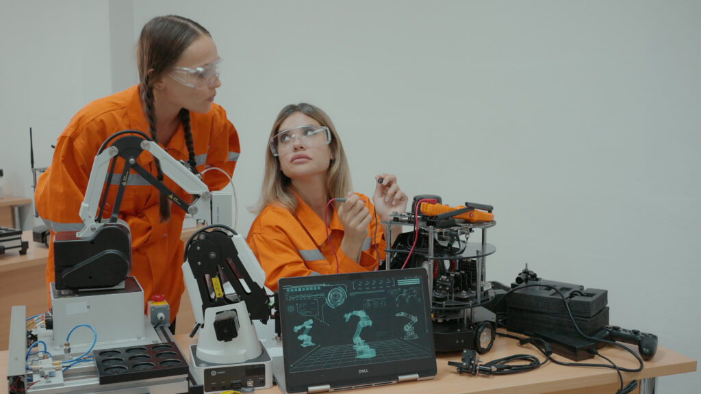 Two engineers wearing orange discussing and creating robotic devices