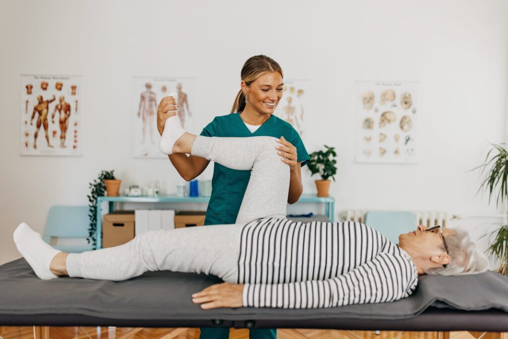 Senior lying on the medical table, exercising legs with assistance of the physiotherapist